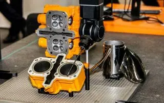 Black CMM arm working on bright orange machine parts
