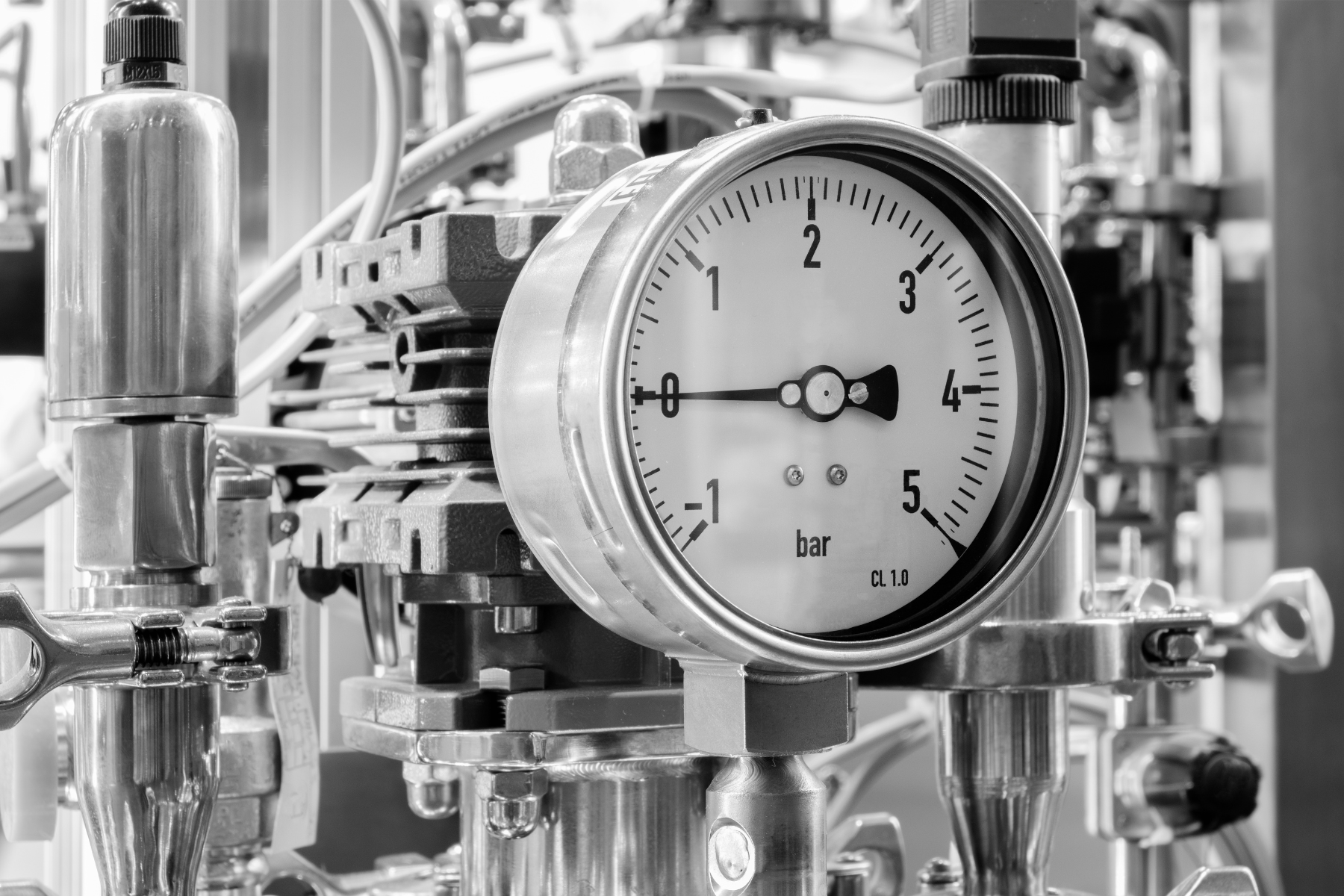 A close-up black-and-white photo of a pressure gauge displaying bar readings on industrial equipment.