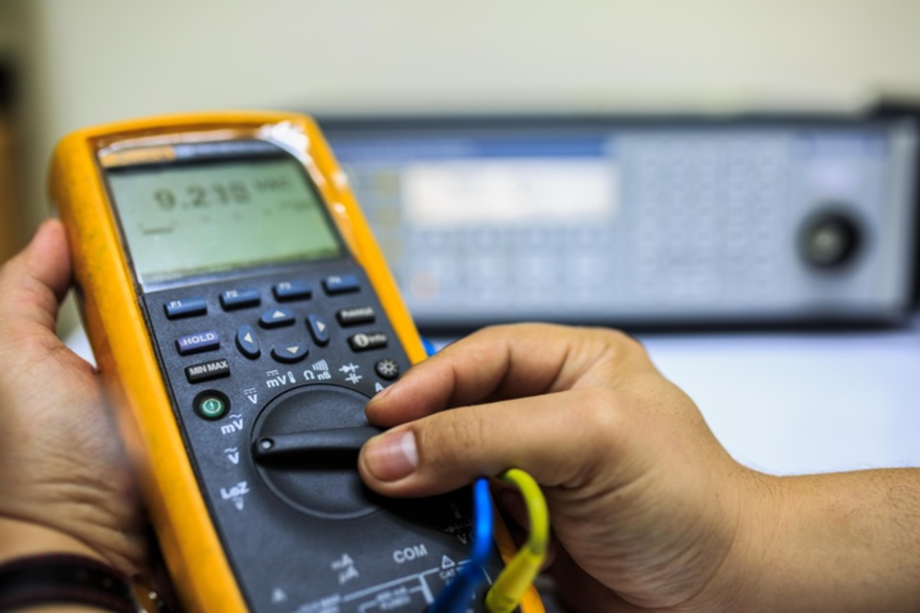Person adjusting the dial on a handheld multimeter for measurement or calibration.