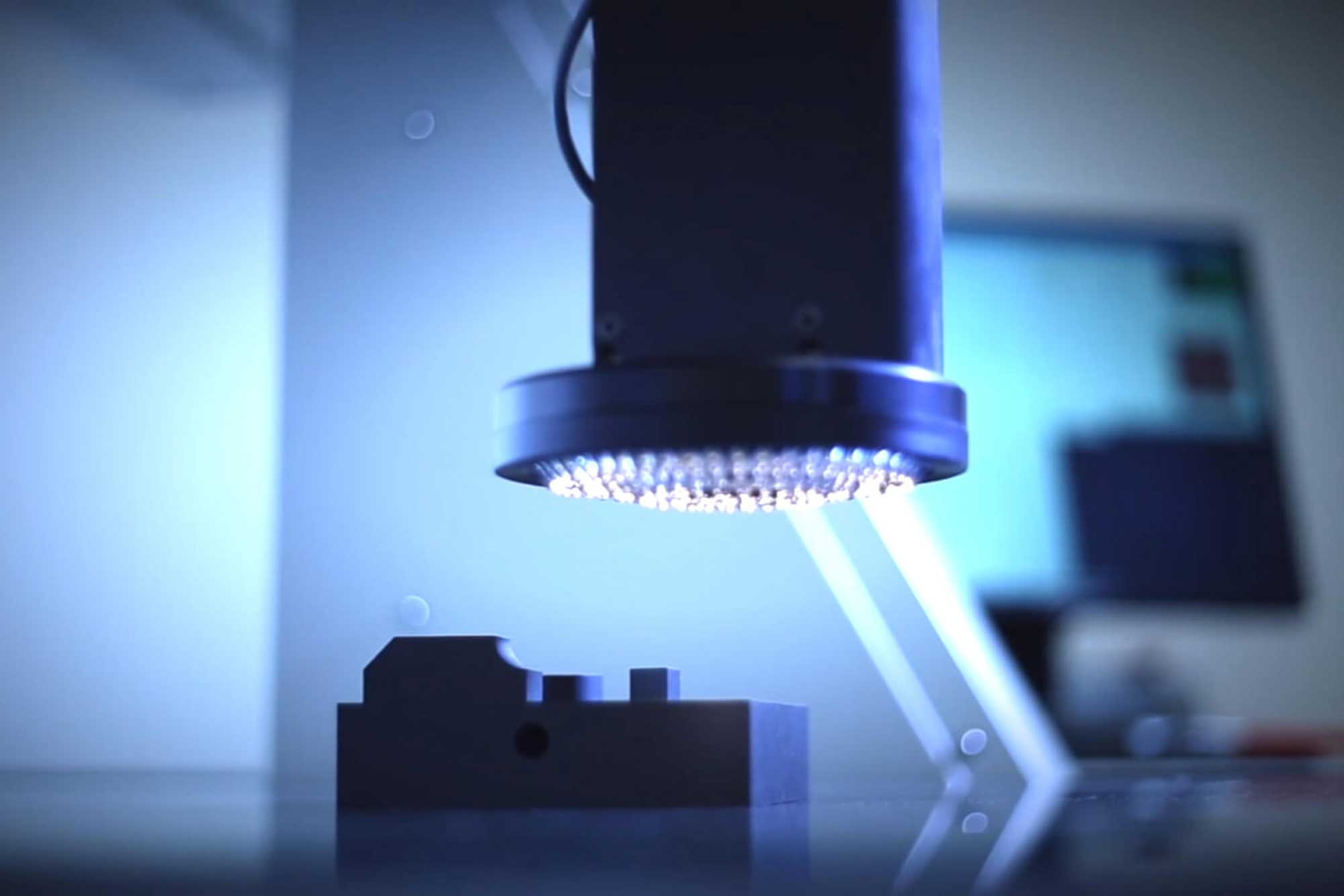 A closer look at a Micro-Vu measuring head with bright lights focused on a small, shaped metal object beneath it.