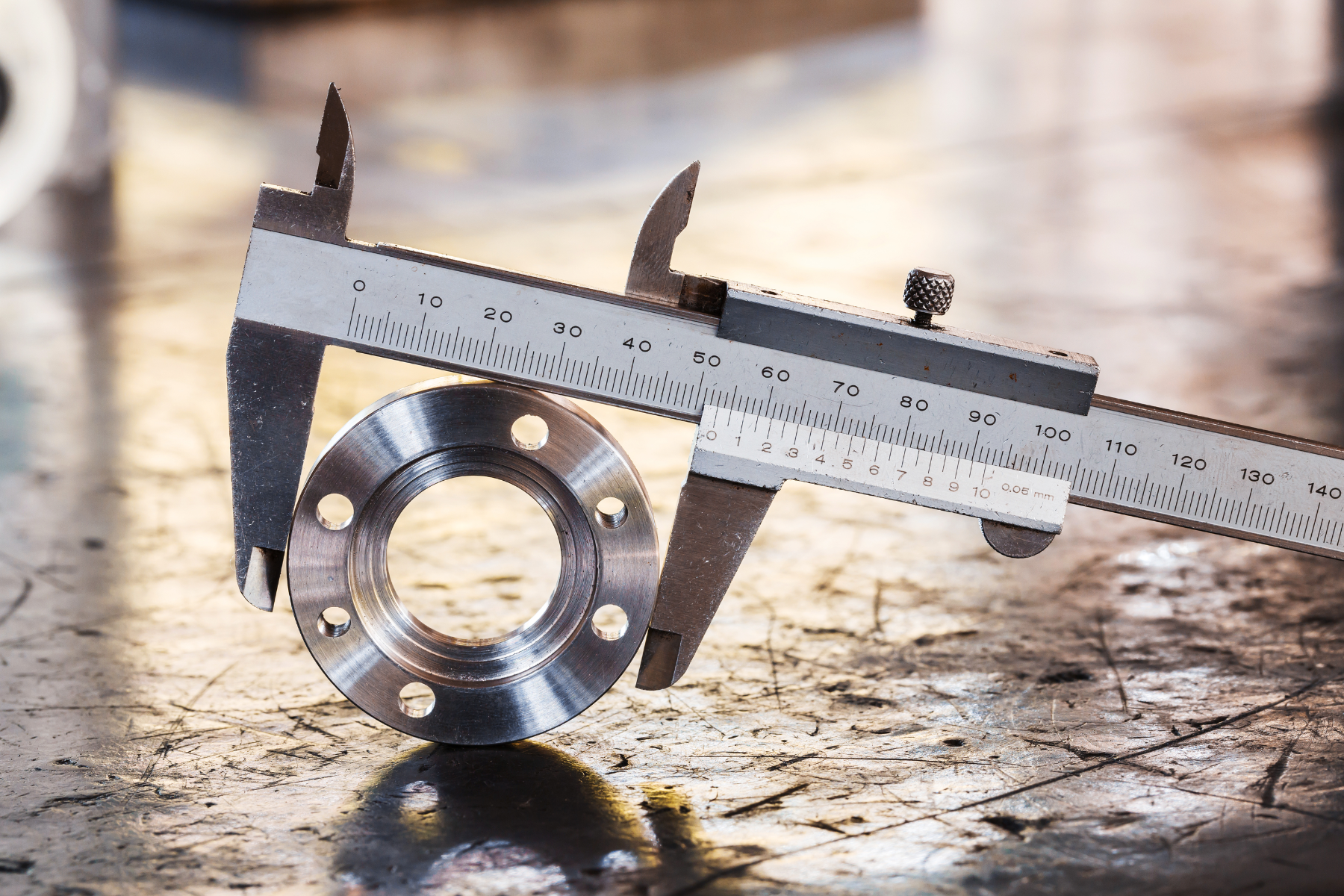 Atraditional vernier caliper measuring the diameter of a circular metal part on a worn workbench. It illustrates hands-on inspection techniques commonly used in workshops to ensure parts meet dimensional specifications.