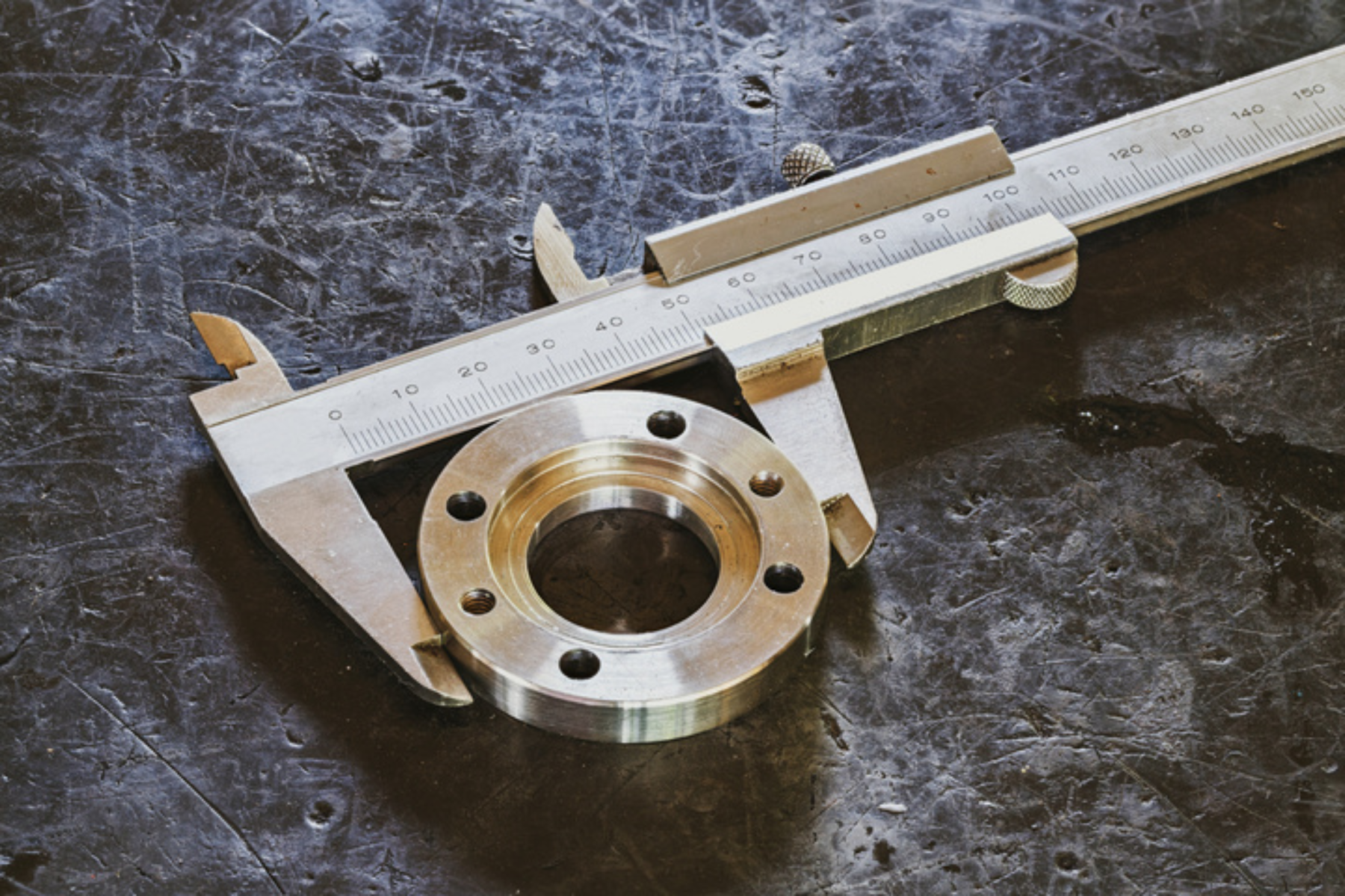 A metal flange part rests on a workbench while a caliper measures its diameter, highlighting precision machining.