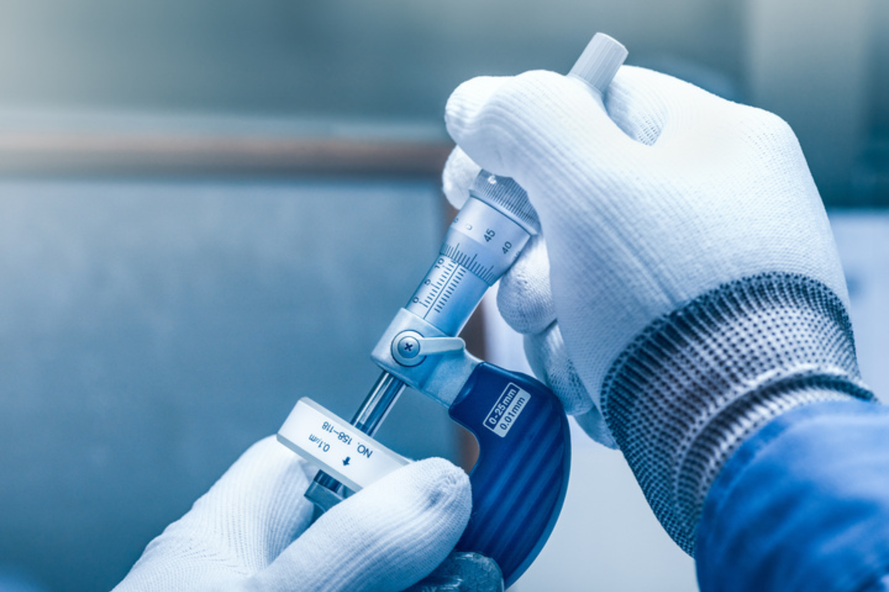 A detailed close-up of gloved hands using a micrometer to measure a small component. The image conveys precision, careful handling, and quality assurance, highlighting hands-on inspection and the importance of accurate dimensional measurement in metrology.